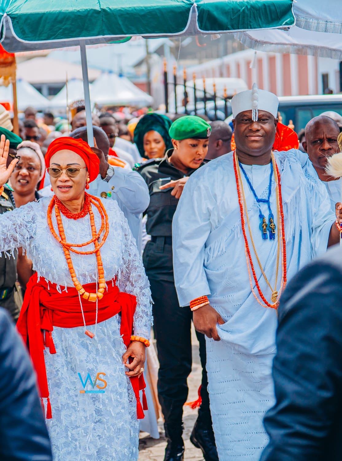 Nigeria's First Lady, Oluremi Tinubu, walks with a Warri chief through the crowd at the palace, under the kingdom's ceremonial umbrellas.